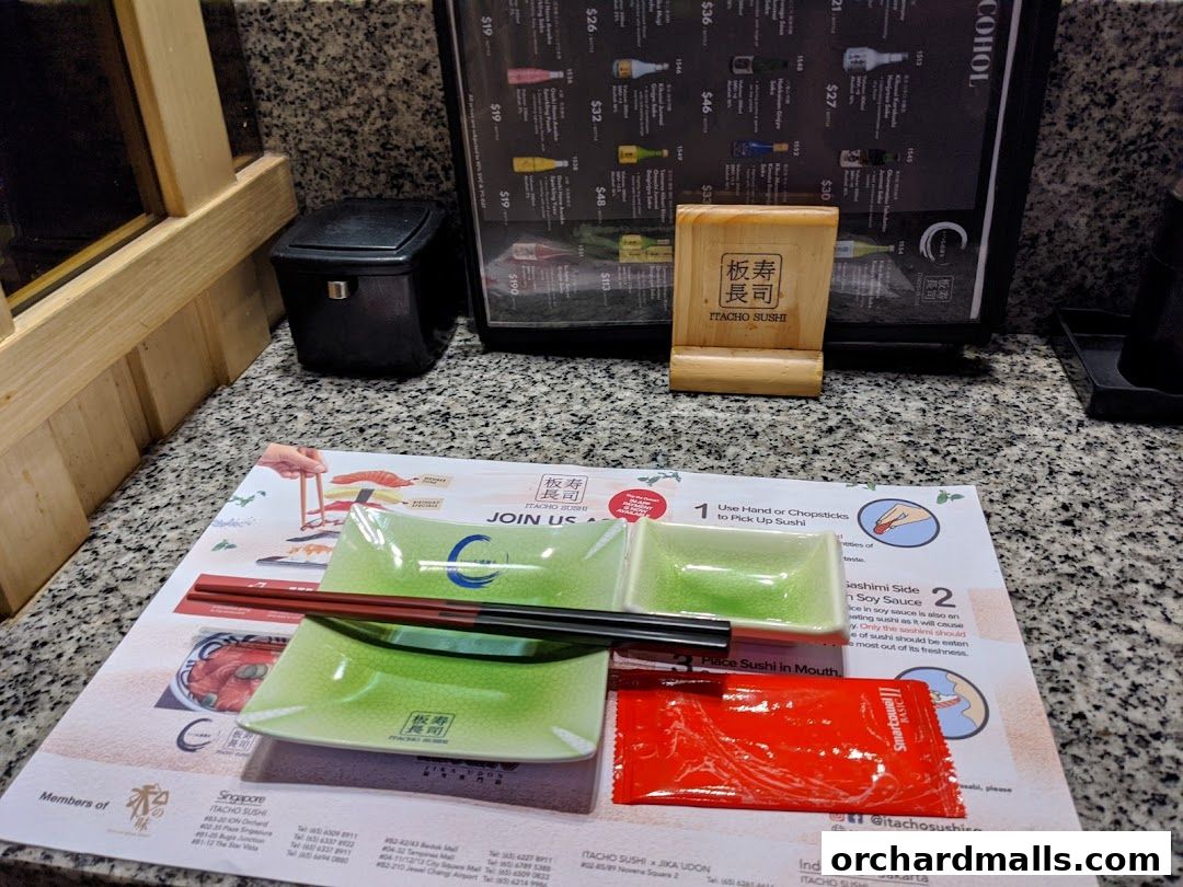 A table setting at Itacho Sushi with chopsticks, soy sauce packets, and a menu stand.