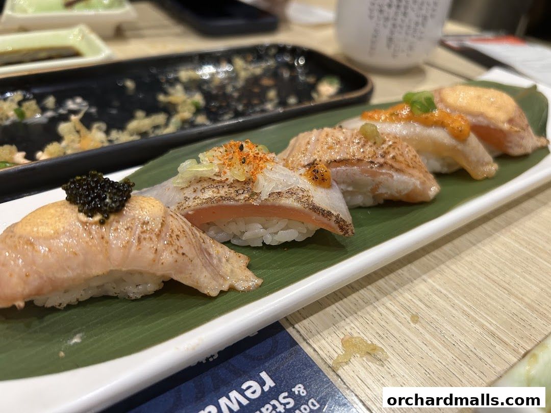 A close-up of five pieces of sushi with various toppings on a white plate with a green leaf.