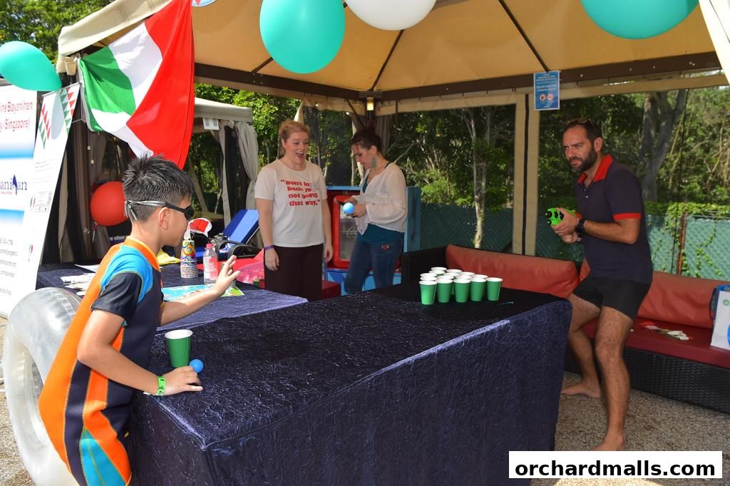 People playing a cup-tossing game at an outdoor event with Italian flags.