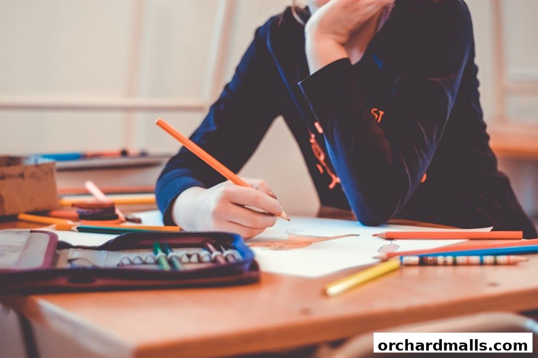 A student draws with colored pencils at a desk in a classroom.