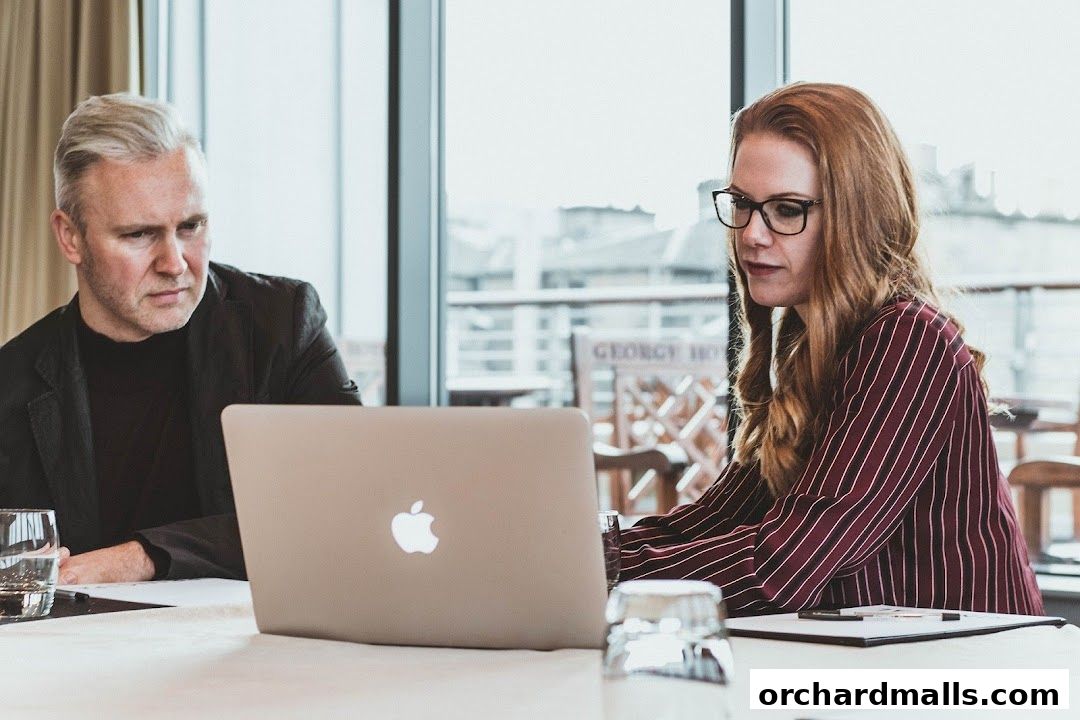 Two professionals, a man and a woman, are looking at a laptop screen.