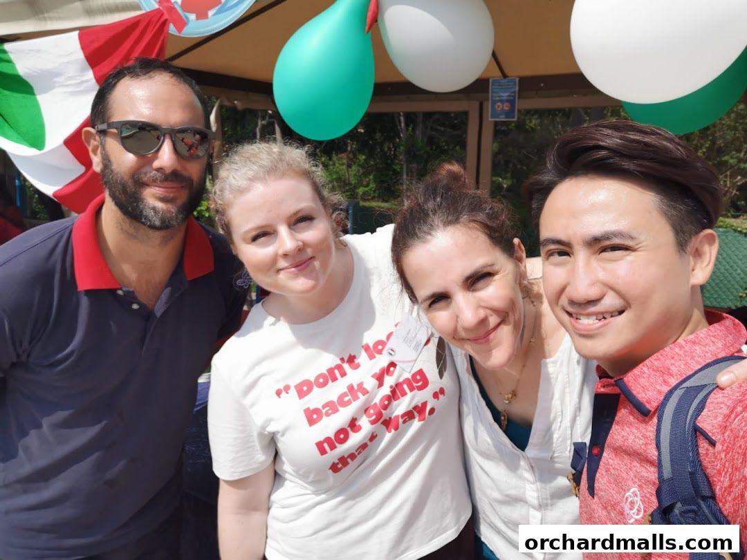 Four smiling people pose for a selfie outdoors with Italian flags and balloons.