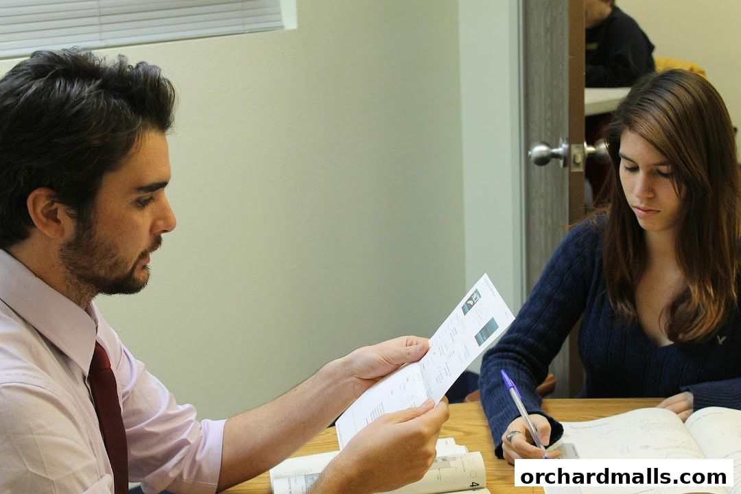 A man shows a document to a woman who is writing in a book.