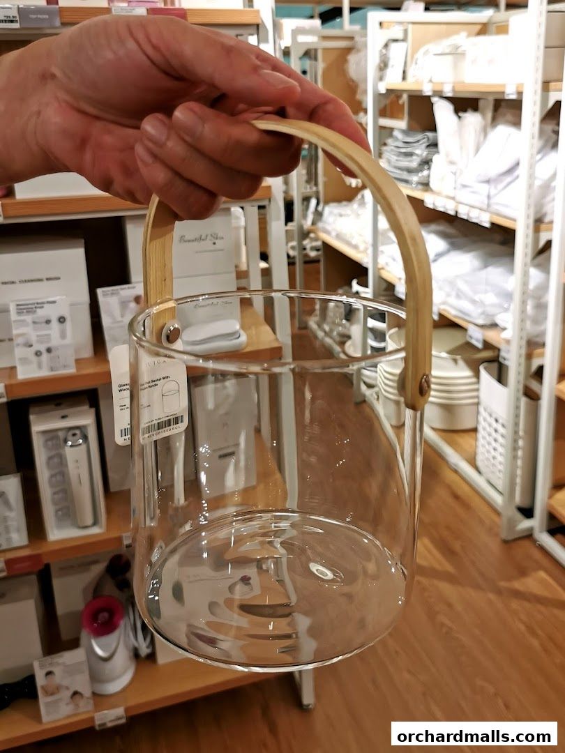 A hand holds a clear glass container with a wooden handle in a retail store.