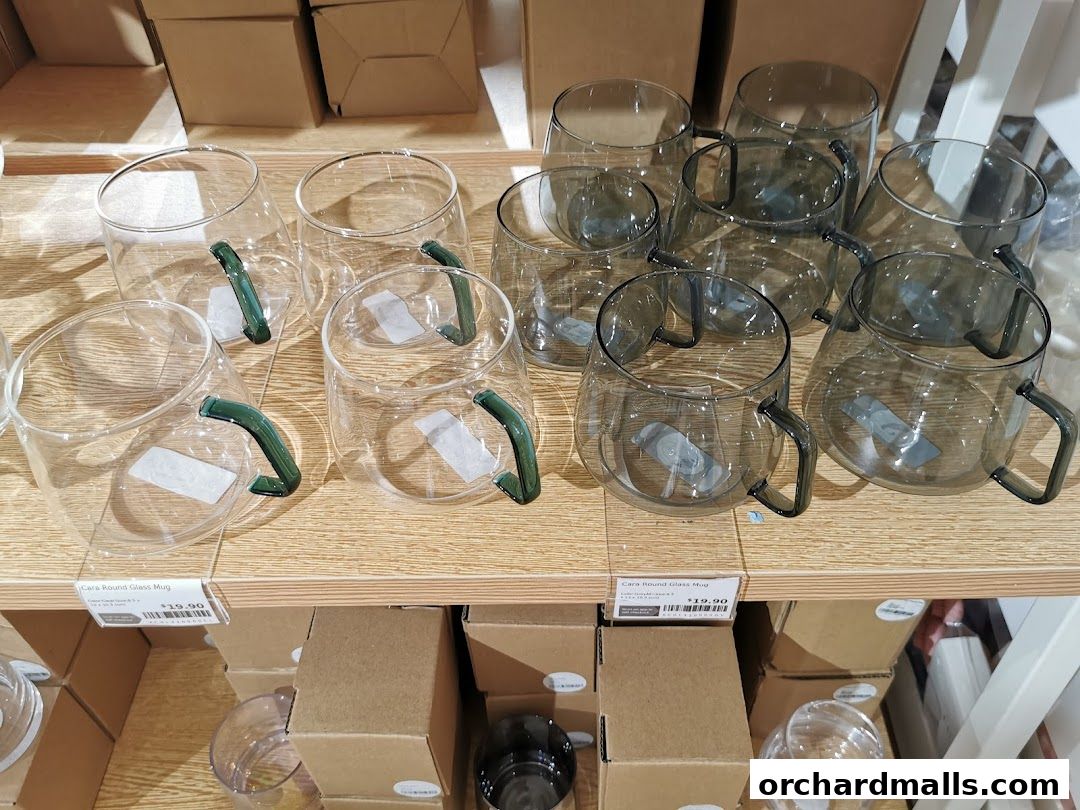 A display of clear and tinted glass mugs with green and dark handles on shelves.