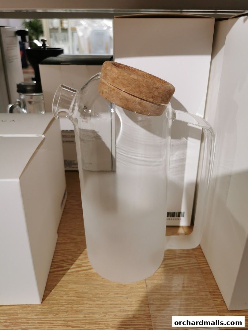 A frosted glass pitcher with a wooden lid sits on a shelf surrounded by white boxes.