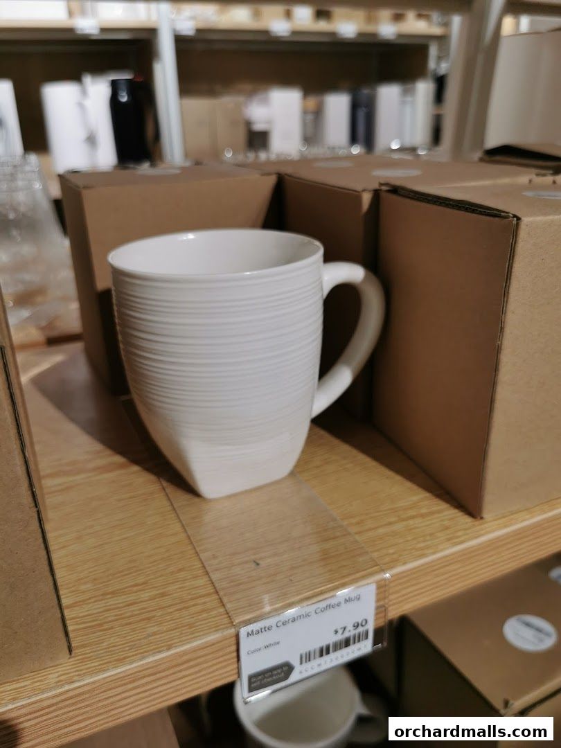 A white matte ceramic coffee mug with a textured design is displayed on a shelf.