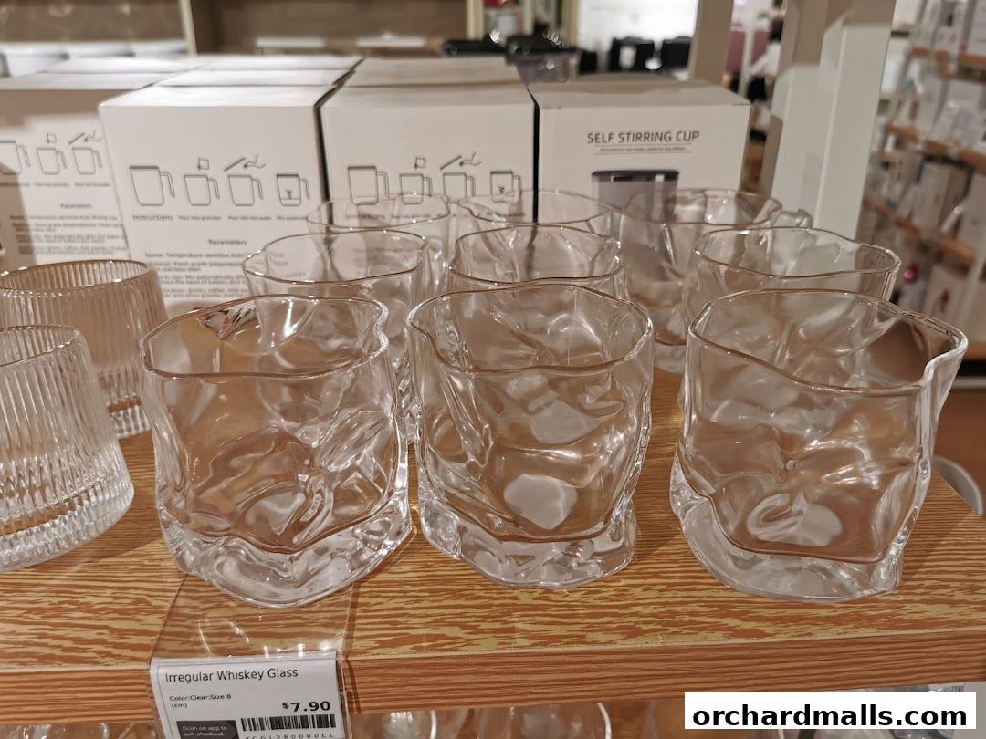 A display of irregular whiskey glasses on a wooden shelf with product boxes in the background.