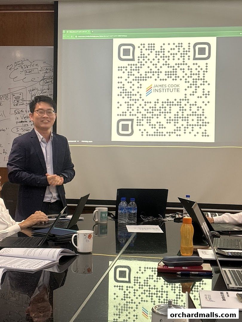 A man in a suit presents a QR code for James Cook Institute on a projector screen.