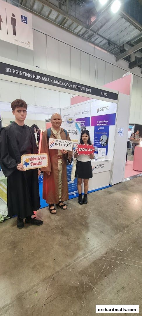 Three people stand at a booth for James Cook Institute, promoting 3D printing and IT workshops.