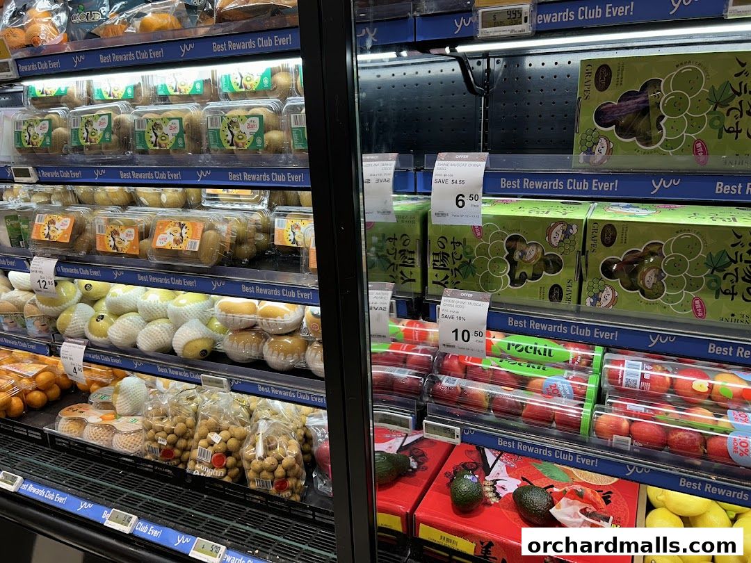 A refrigerated display case filled with various fresh fruits like grapes, kiwis, apples, and avocados.
