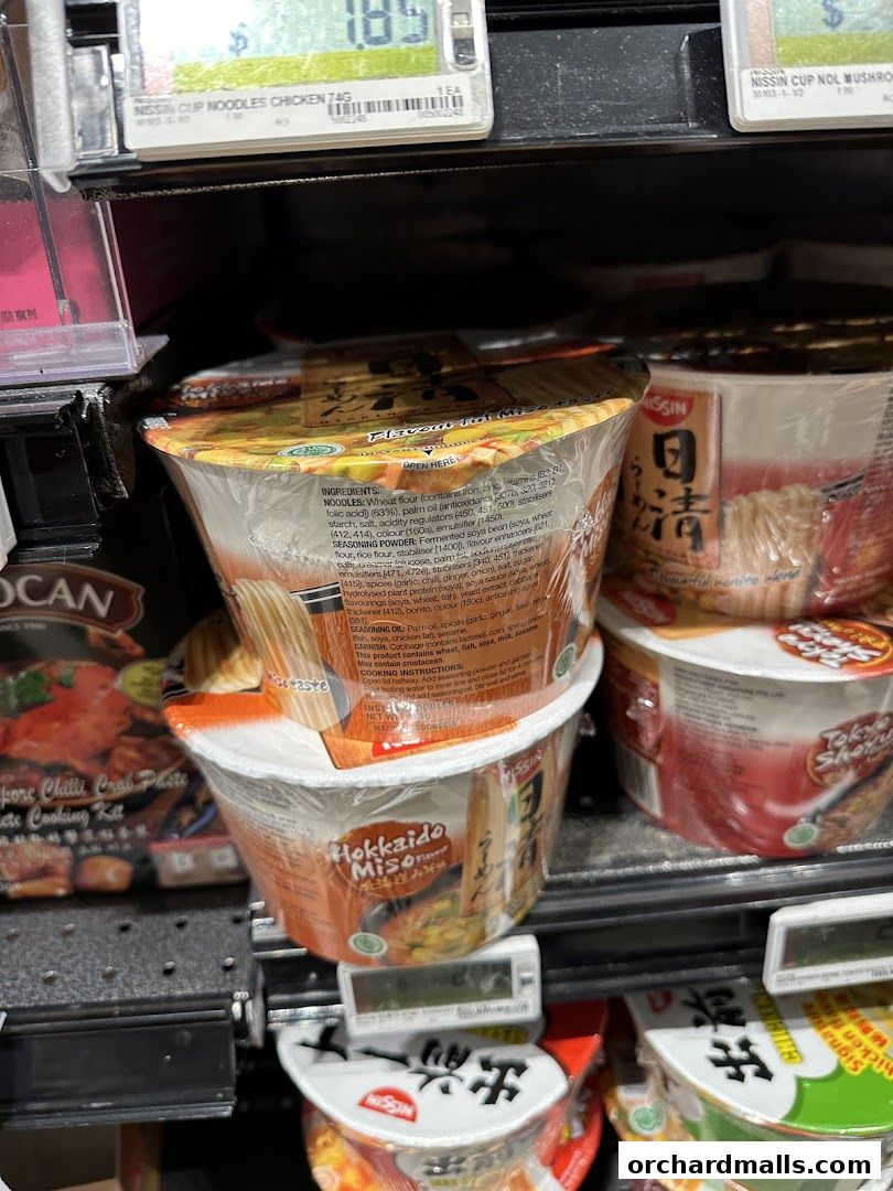 A shelf in a store displaying various Nissin cup noodles, with prices visible.