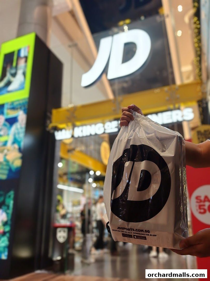 A person holds a JD King of Trainers shopping bag in front of the store.