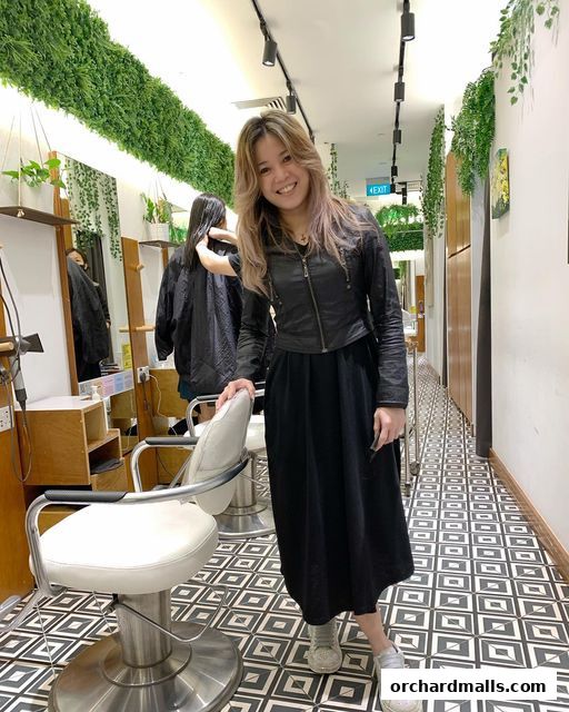 A smiling woman stands in a modern salon with lush greenery and stylish chairs.
