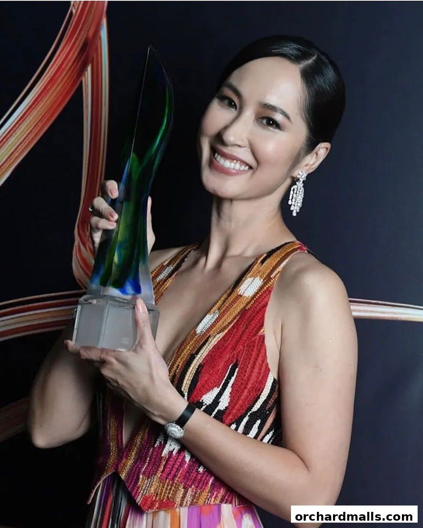 A smiling woman in a colorful dress holds a glass award.