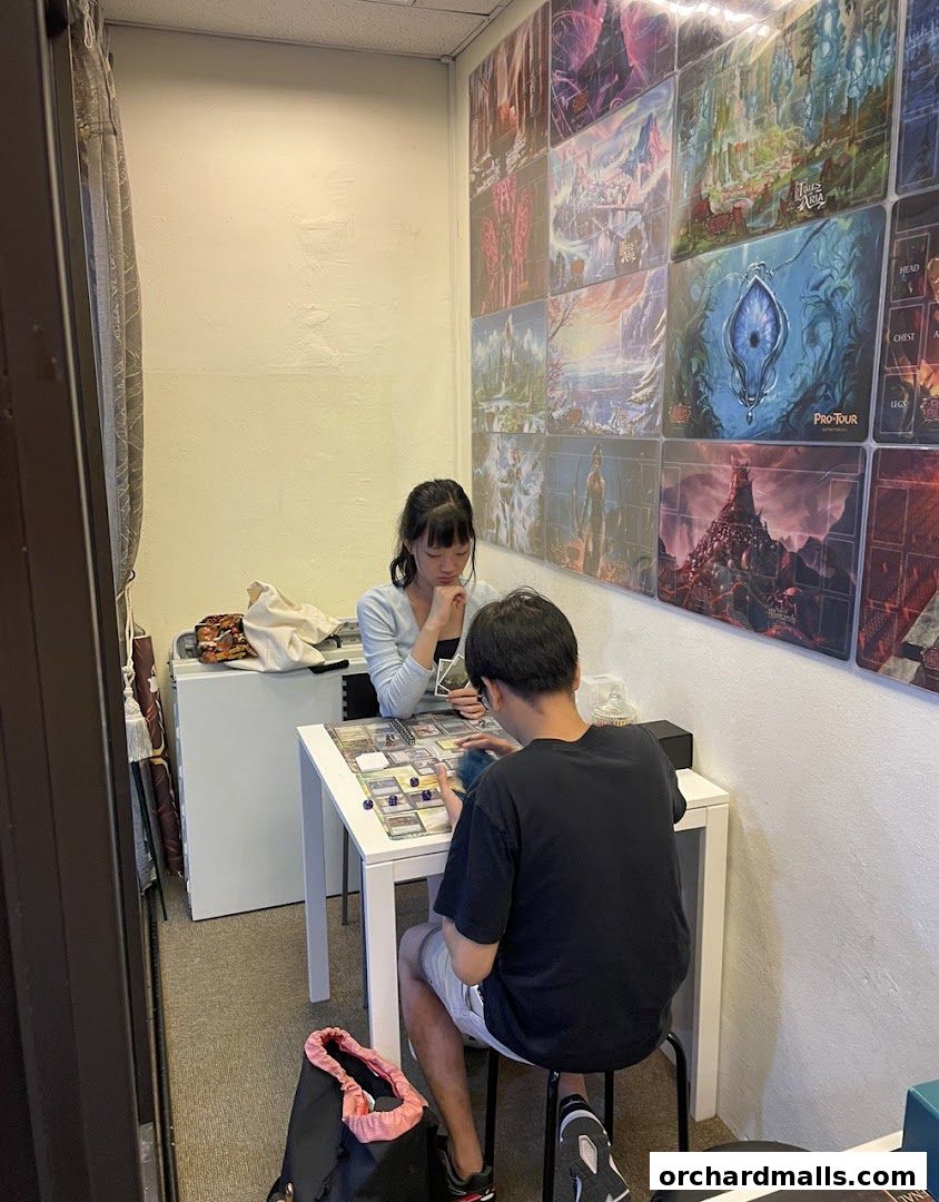 Two people playing a board game at a table in a shop with fantasy art on the walls.