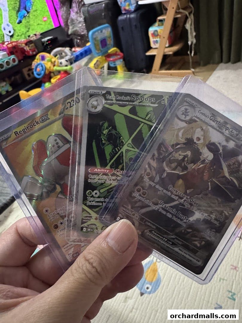 A hand holds three collectible Pokémon trading cards: Regirock EX, Team Rocket's Spidops, and Cynthia's Garchomp.