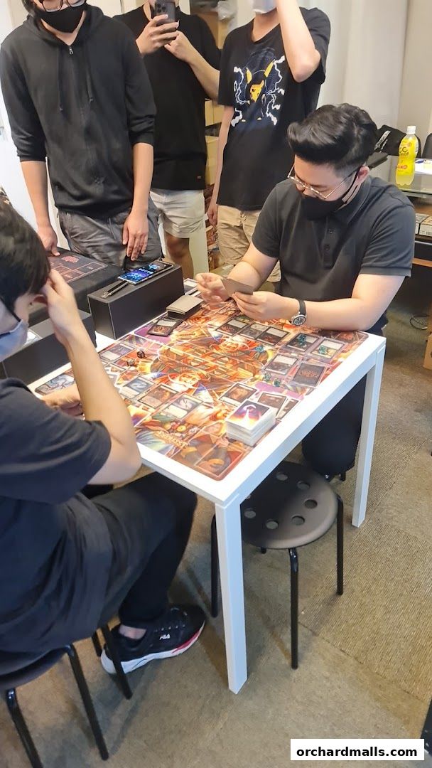 People playing a card game at a table covered with game cards and accessories.