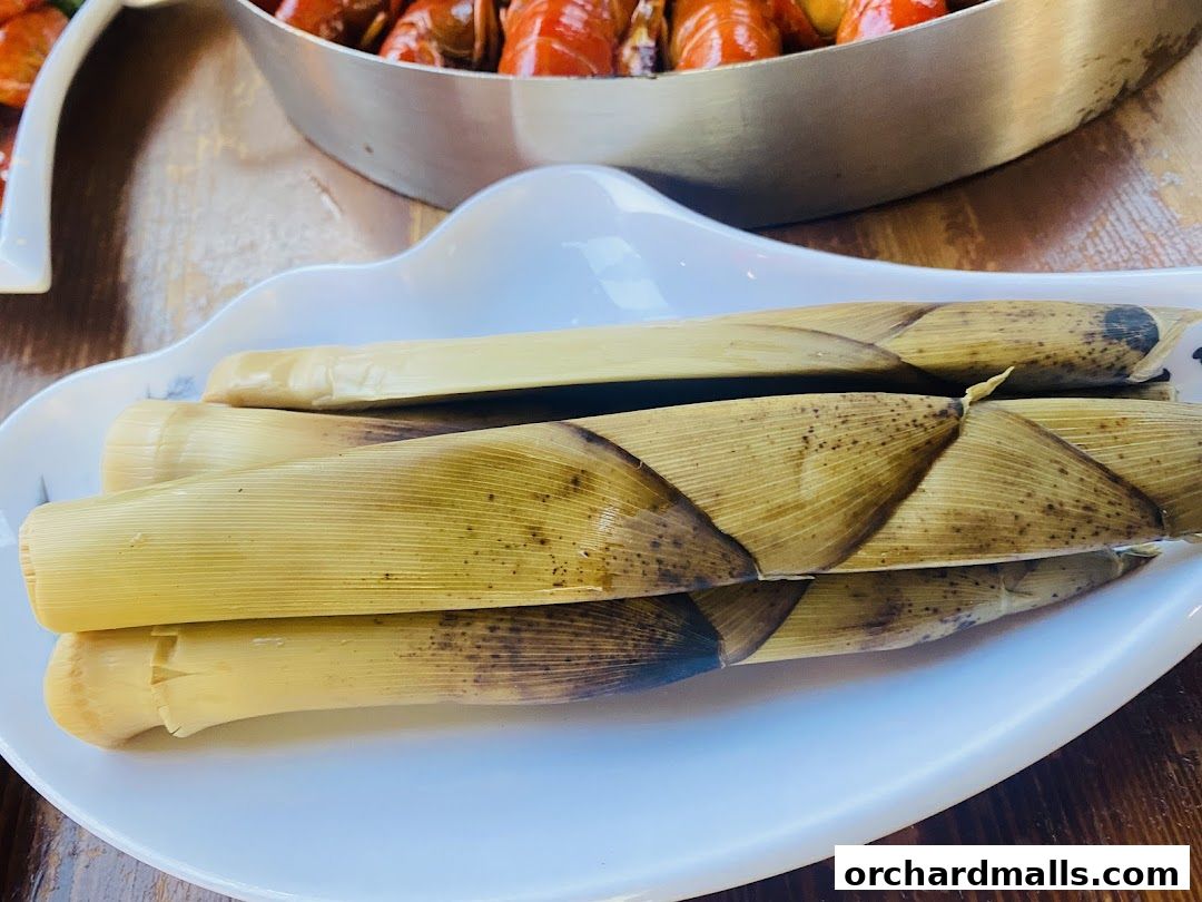 A close-up of fresh bamboo shoots served on a white plate, with crawfish in the background.