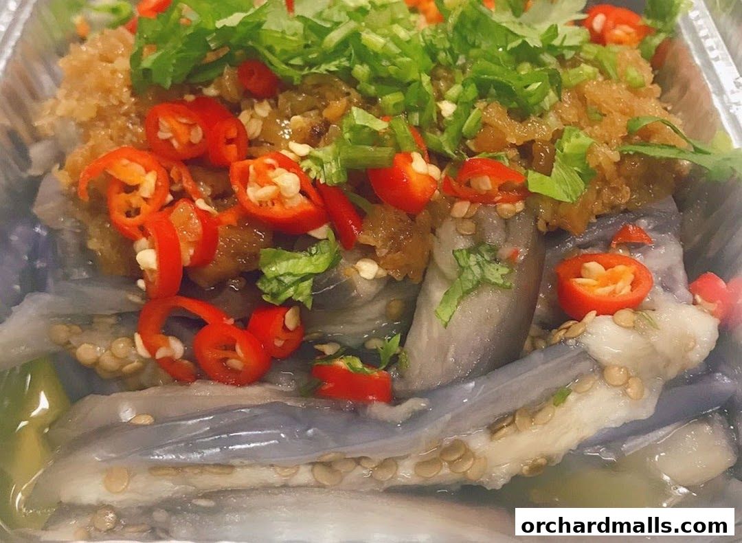 A close-up of a dish featuring steamed eggplant with chili, garlic, and cilantro.