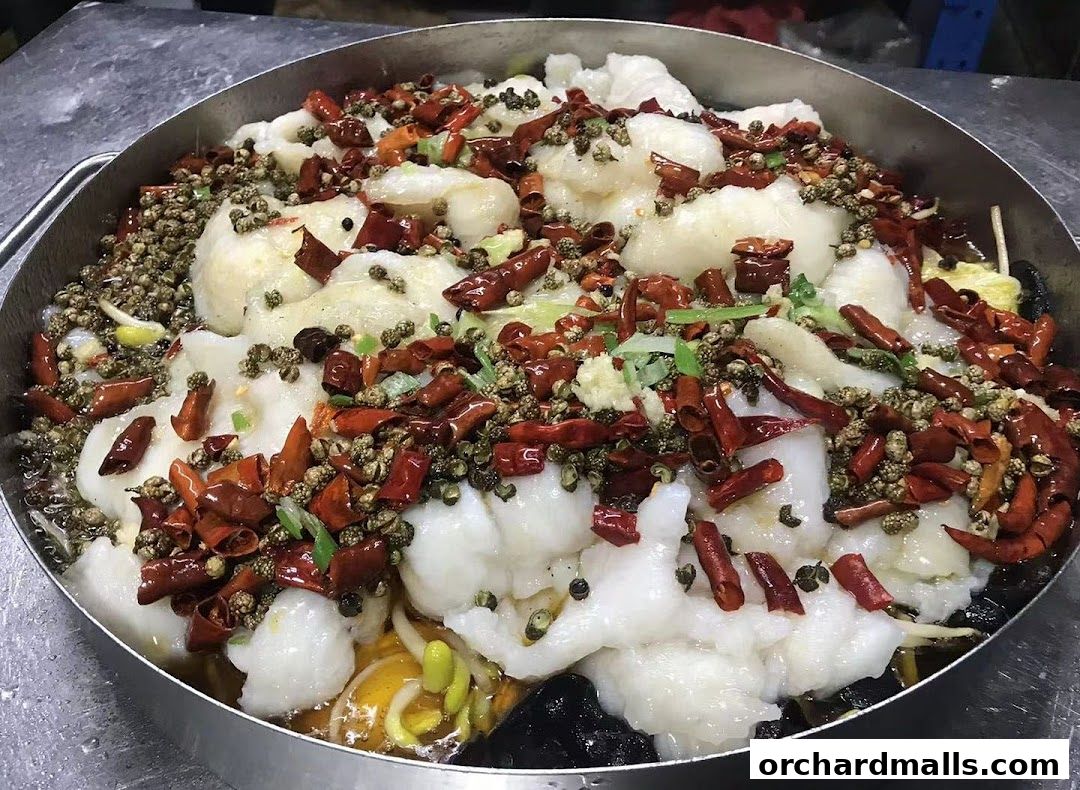 A close-up of a large metal bowl filled with tender fish, dried chilies, and Sichuan peppercorns.
