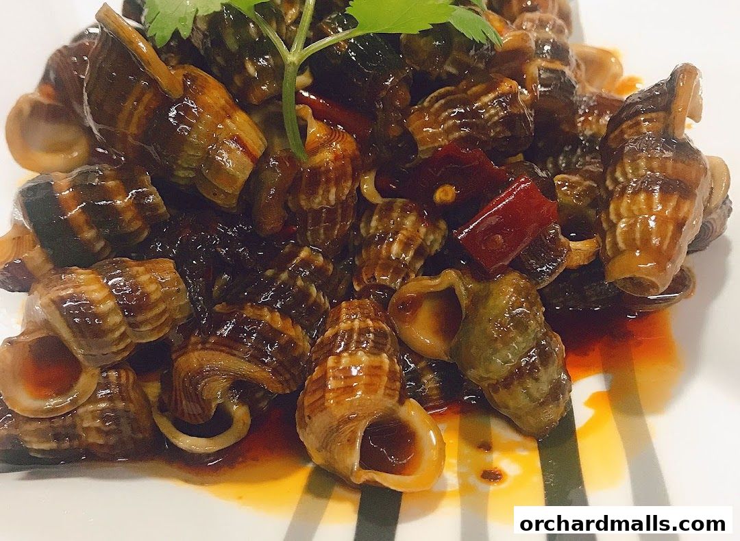 A close-up of a plate of savory snails cooked in a rich, dark sauce with chili peppers and herbs.
