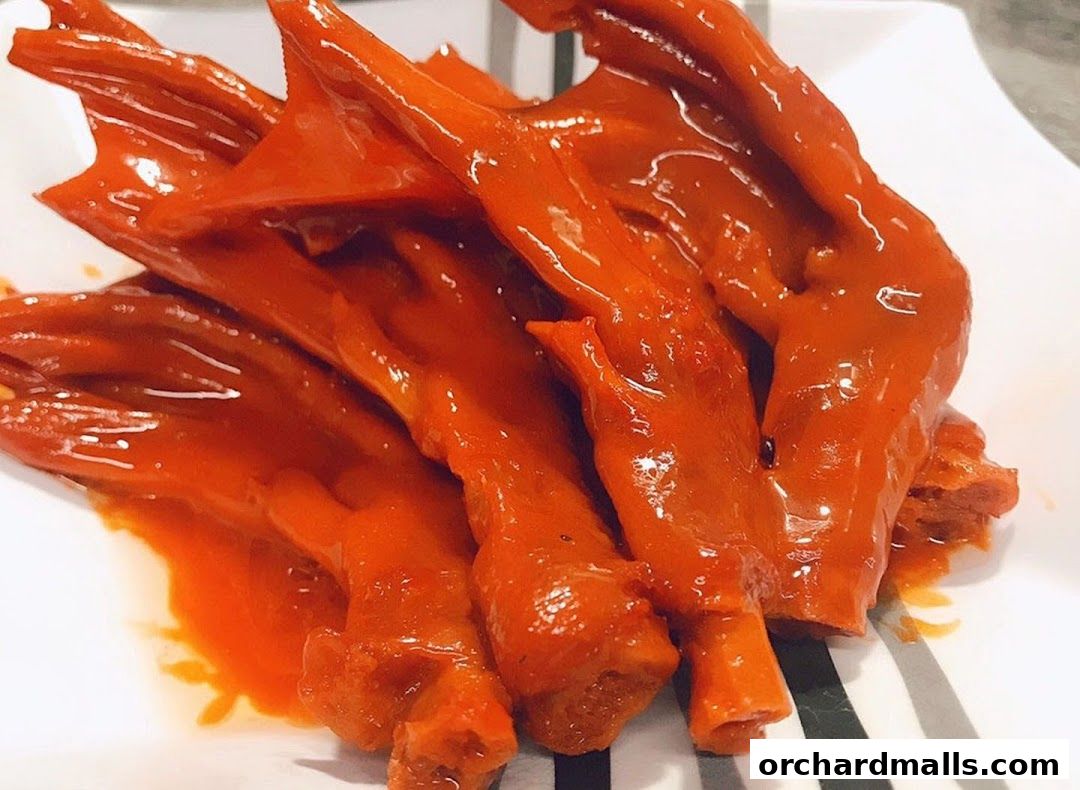 A close-up shot of braised duck feet in a vibrant orange sauce on a white plate.