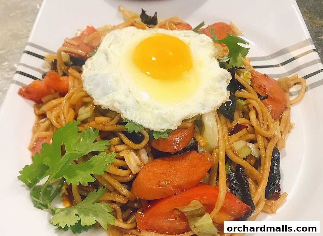 A plate of stir-fried noodles topped with a fried egg, sausage, and vegetables.