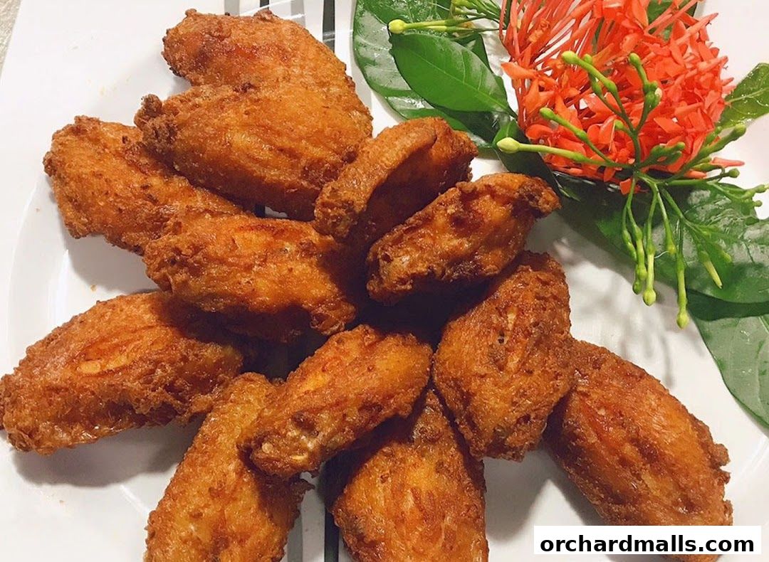 A plate of golden-brown fried chicken wings garnished with green leaves and red flowers.