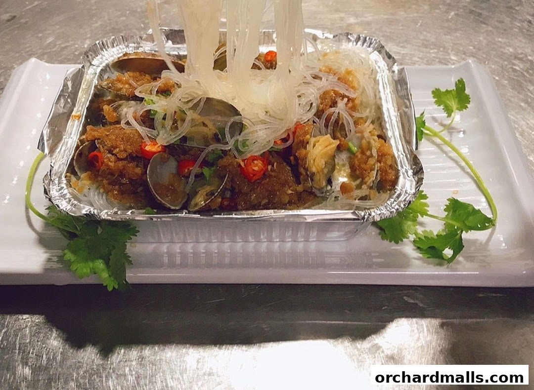 A close-up of a dish featuring clams and glass noodles, garnished with chili and cilantro.