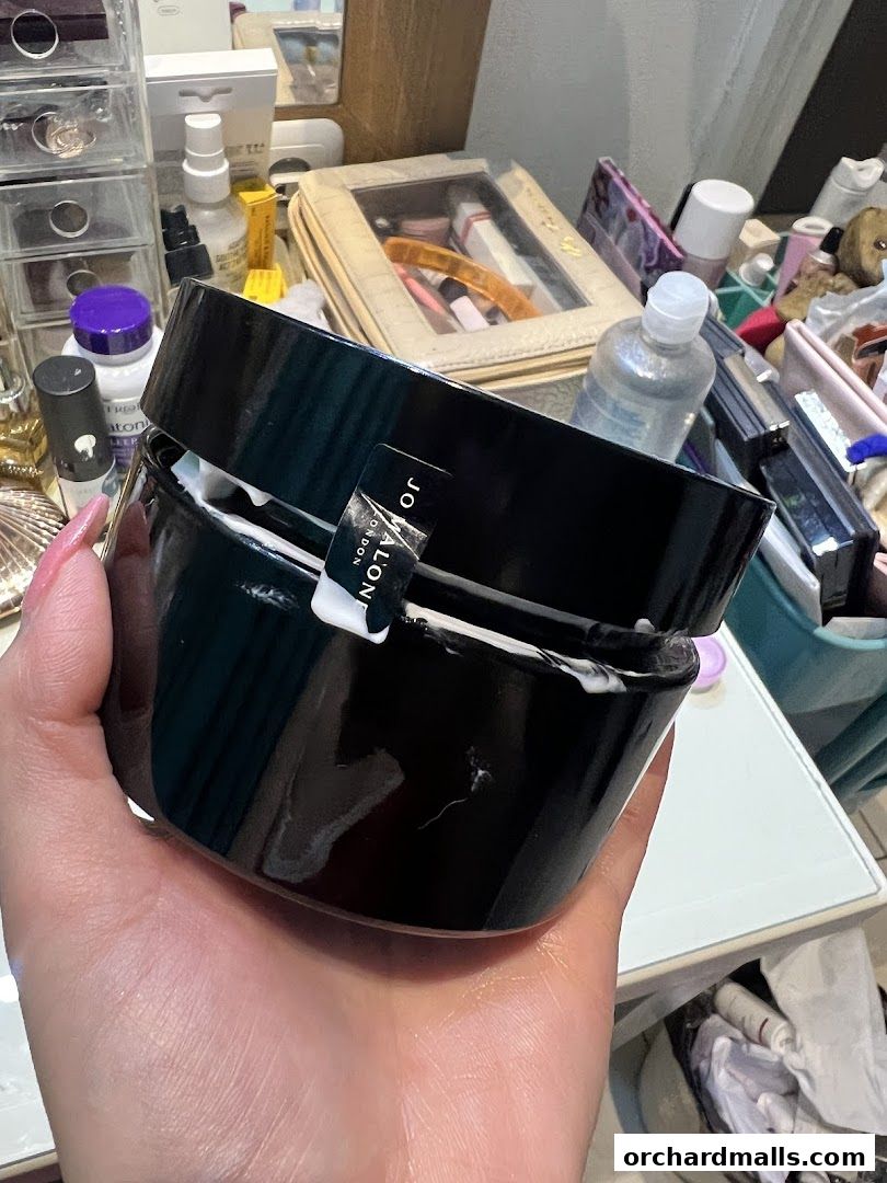 A hand holds a Jo Malone London scented candle in a black jar.