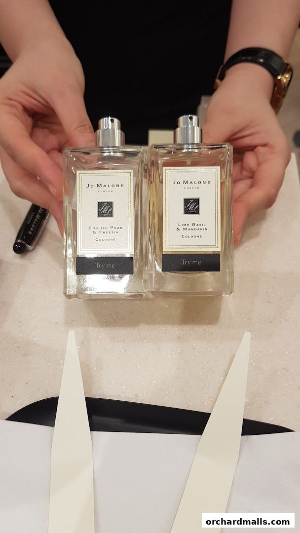 Hands holding two Jo Malone London cologne bottles, English Pear & Freesia and Lime Basil & Mandarin.