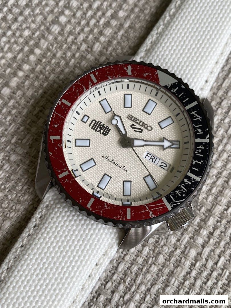 A close-up of a Seiko automatic watch with a textured dial and a red and black bezel.