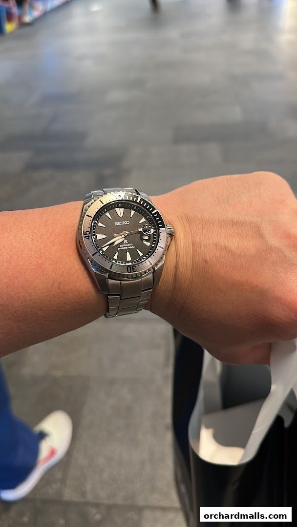 A person wearing a silver Seiko automatic diver's watch and holding a shopping bag.