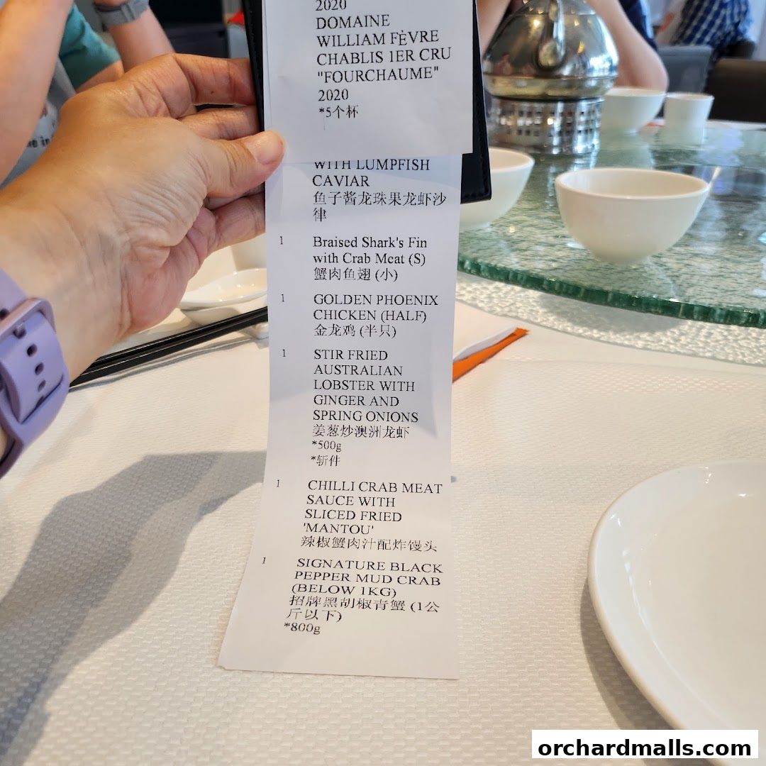 A hand holds a receipt with a list of seafood dishes and wine.