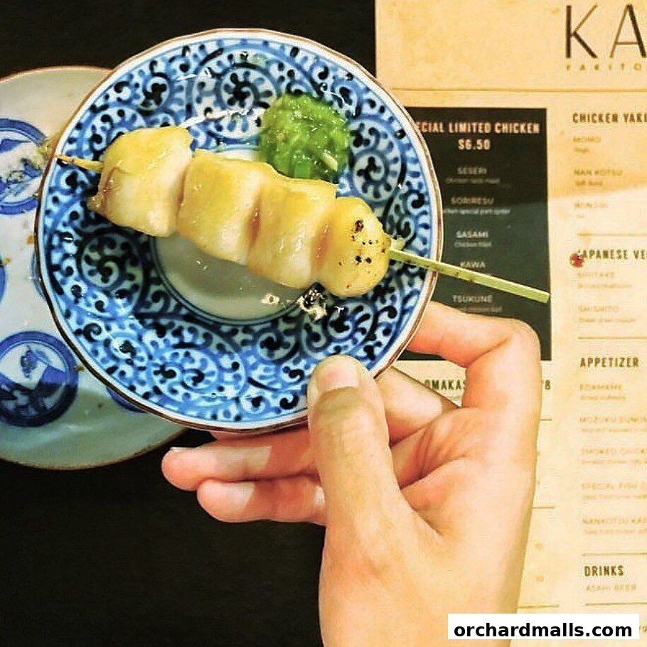 A hand holds a skewer of yakitori in front of a KAI Yakitori menu.