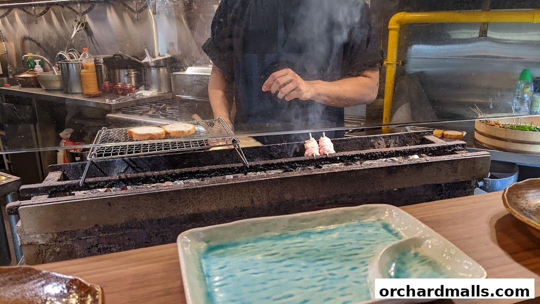 A chef grills skewers and bread over charcoal at KAI Yakitori.
