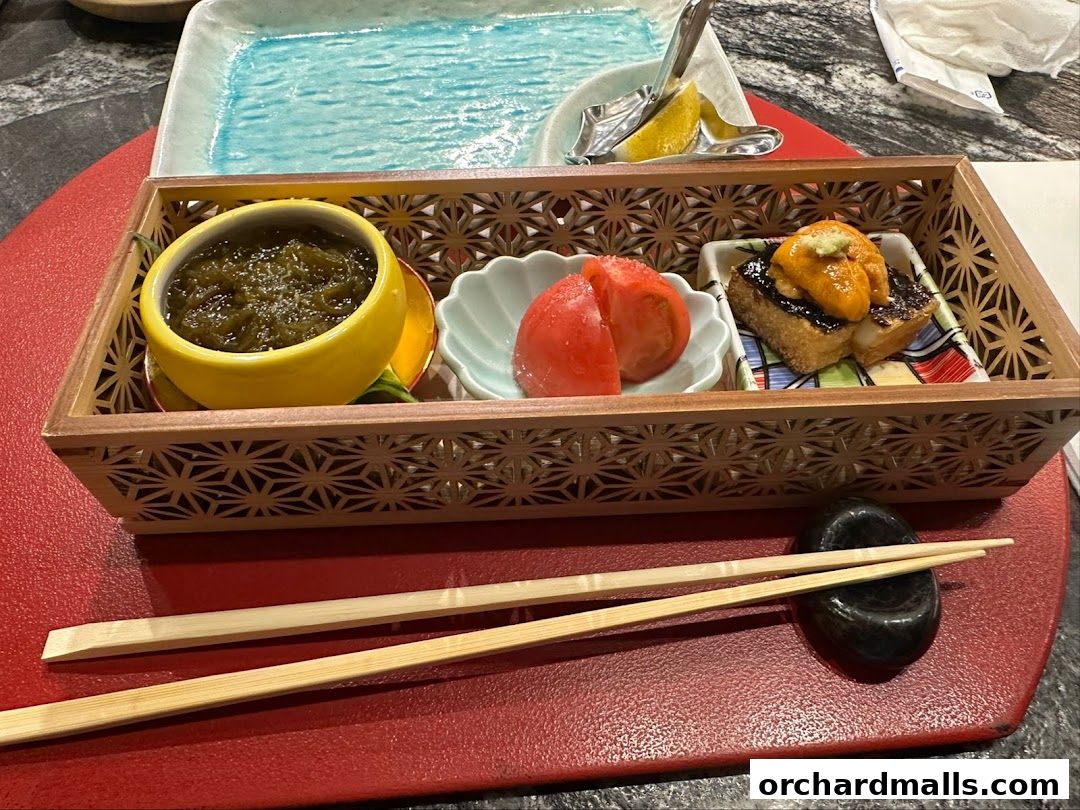 A beautifully presented Japanese appetizer with sea urchin, tomatoes, and a green dish.