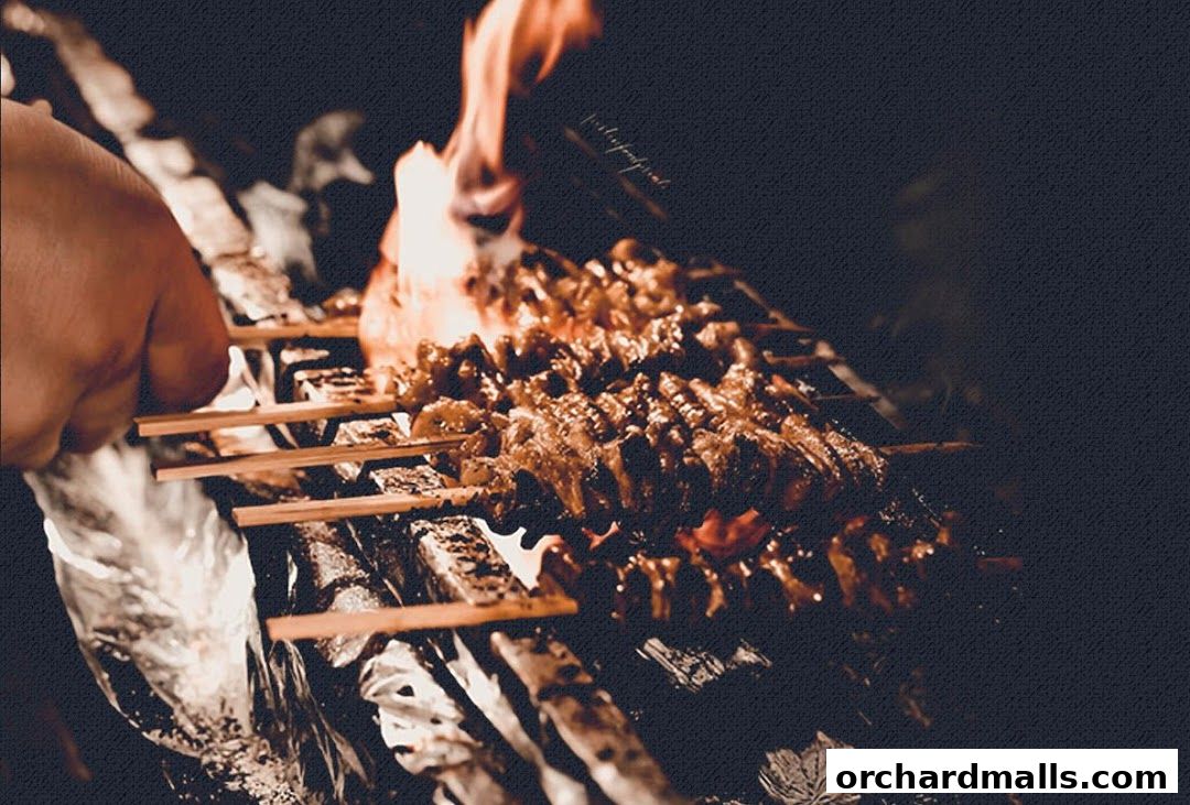 Skewers of yakitori grilling over flames with a hand tending to them.