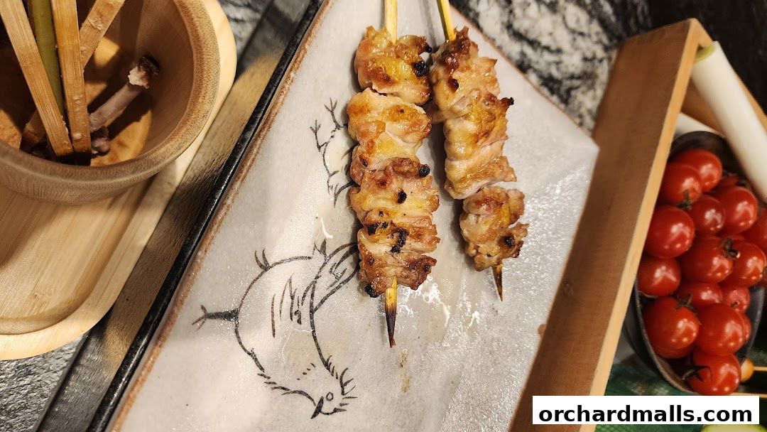 Two skewers of grilled chicken yakitori served on a decorative plate with cherry tomatoes.