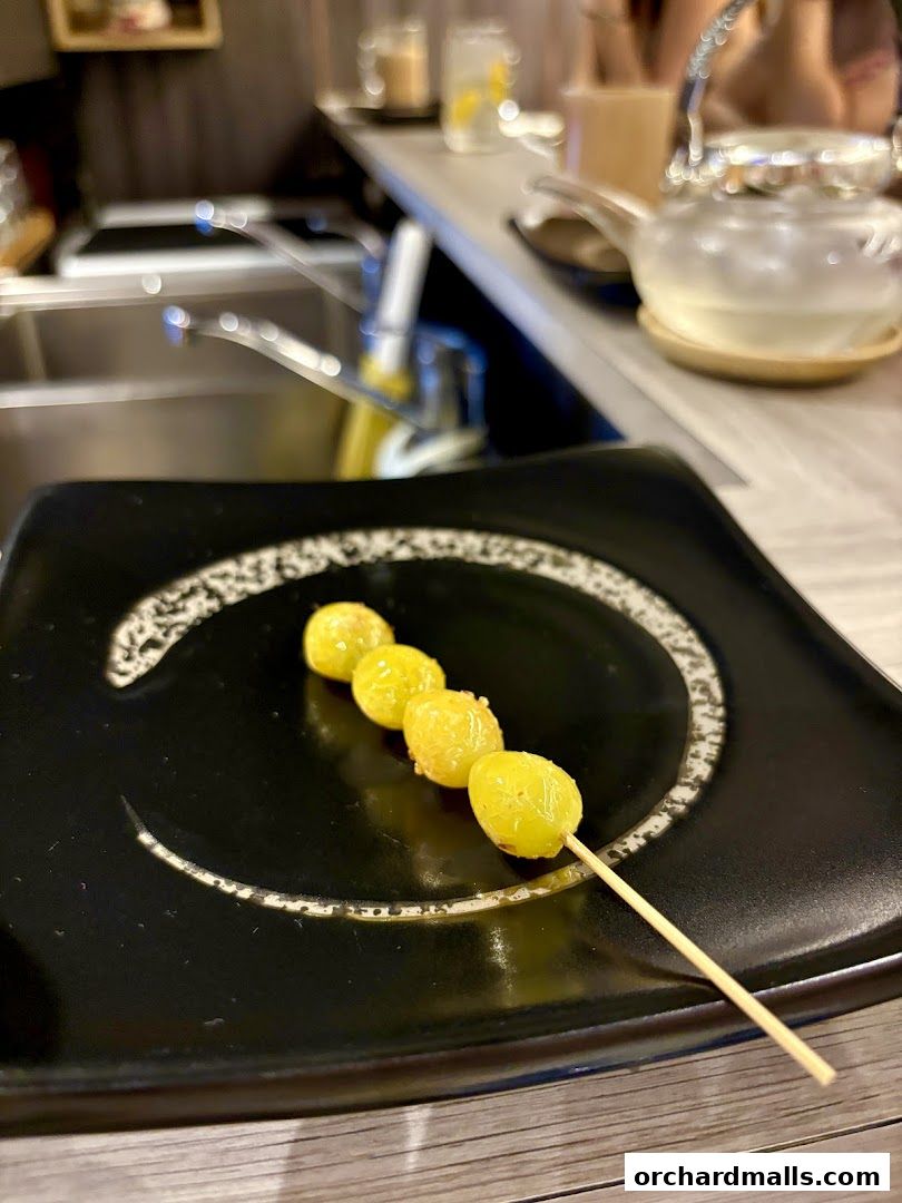 A skewer of golden ginkgo nuts served on a black plate at KAI Yakitori.