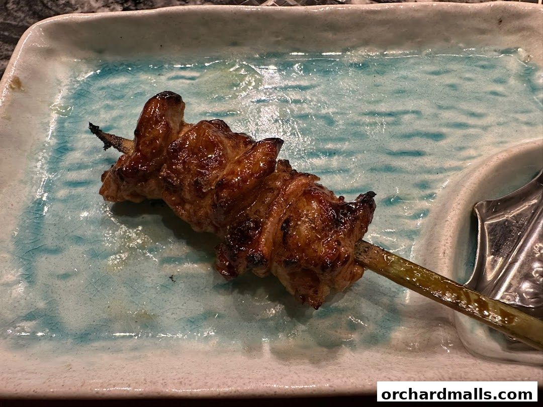 A close-up shot of a perfectly grilled yakitori skewer on a decorative plate.