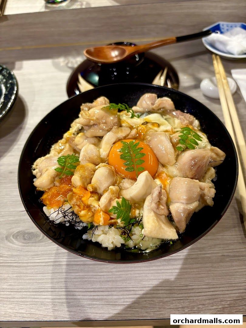 A delicious bowl of Oyakodon with chicken, egg, and rice, garnished with fresh greens.