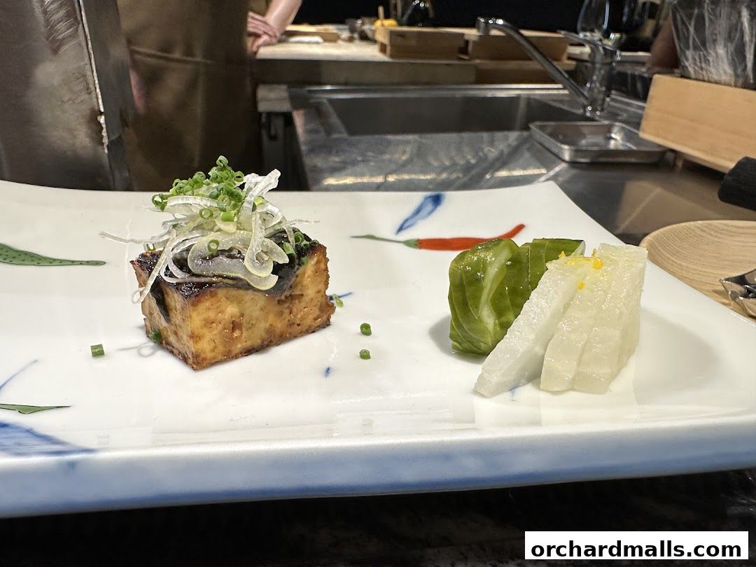 A beautifully presented yakitori dish with grilled eggplant and pickled vegetables on a decorative plate.