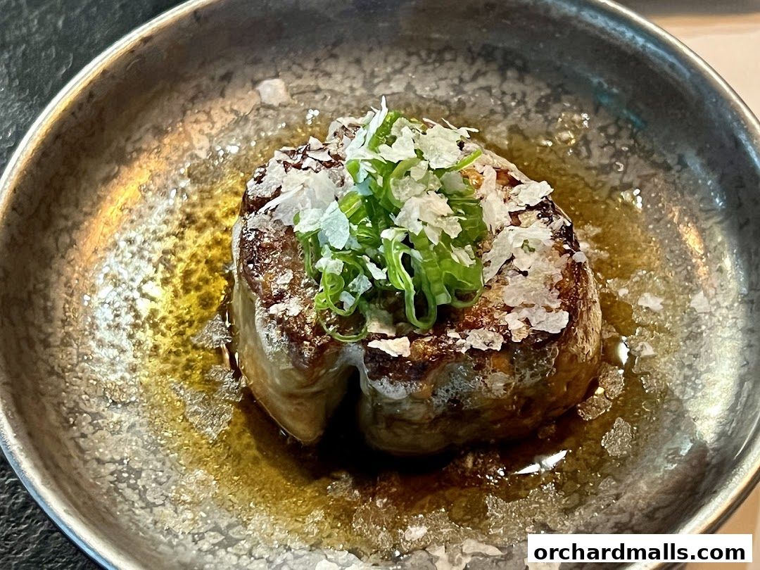 A close-up of a perfectly seared piece of foie gras, garnished with green onions and sea salt.