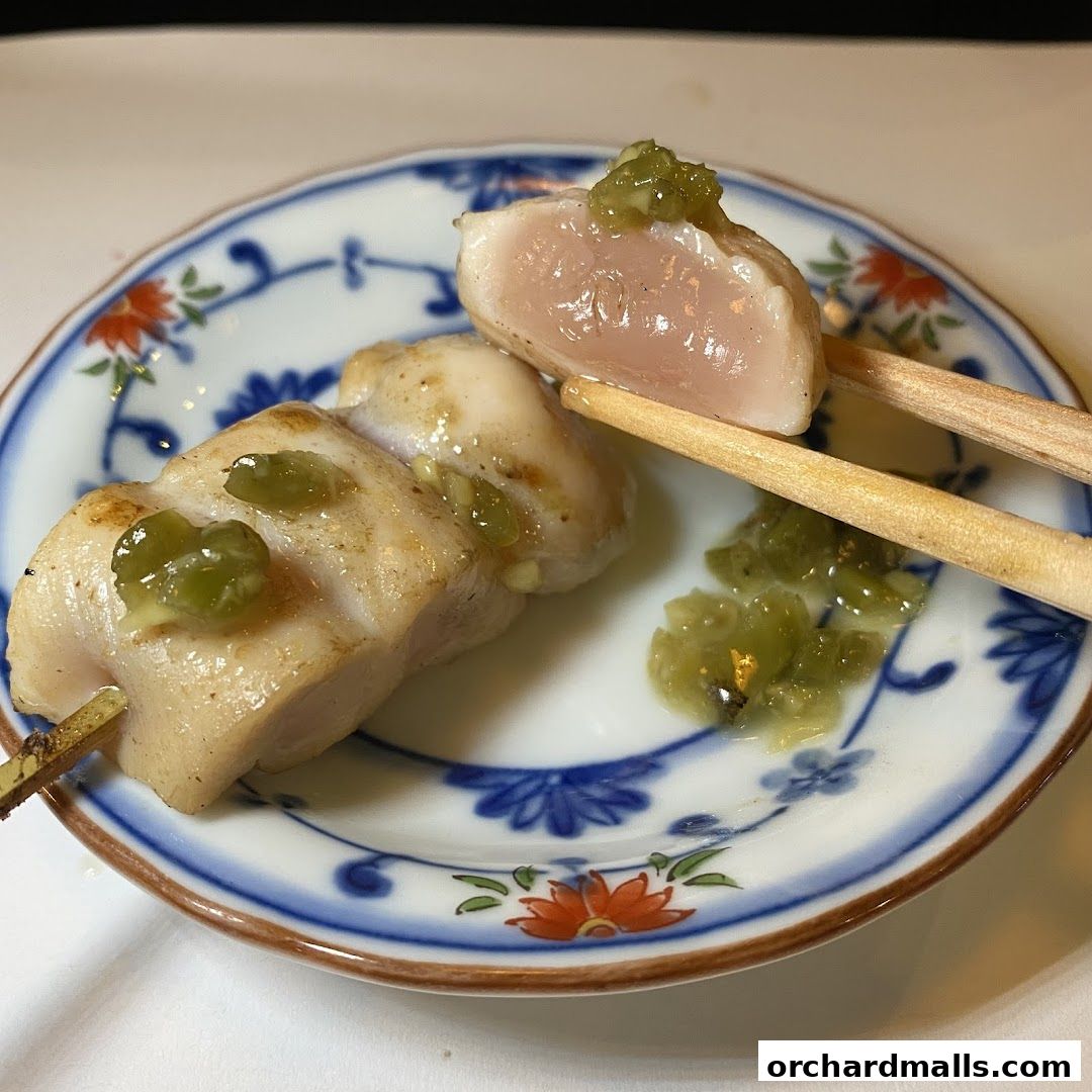 A close-up of a delicious yakitori skewer with green relish on a decorative plate.