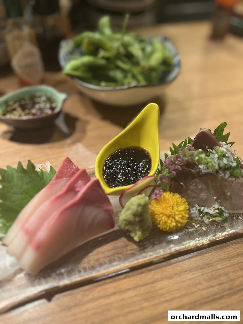 A close-up of a sashimi platter with edamame and dipping sauces.