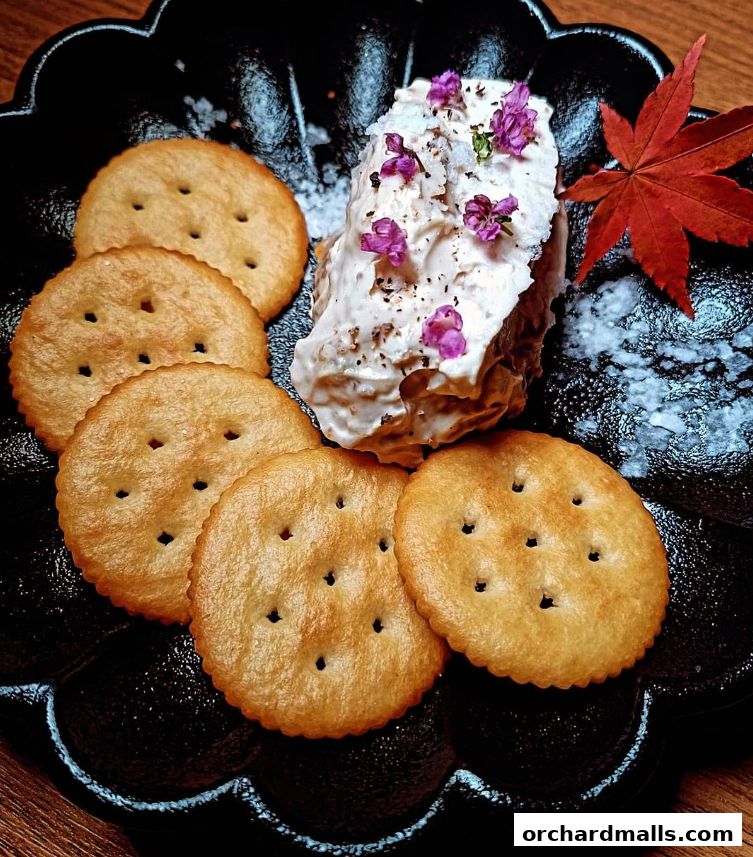 A close-up of a creamy dip served with crackers and garnished with edible flowers.