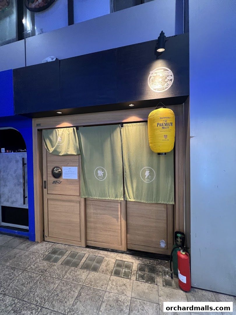 The entrance of Kakiin Oyster Bar features wooden doors, green curtains, and a yellow lantern.
