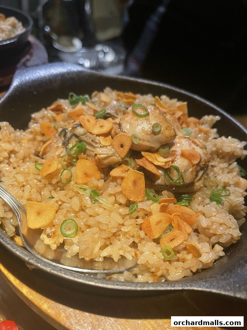 A close-up of a dish featuring rice, oysters, fried garlic, and green onions.
